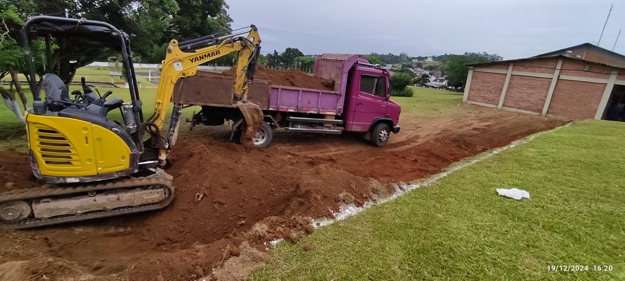 Mini escavadeira amarela da Escava preparando um terreno junto ao caminhão roxo