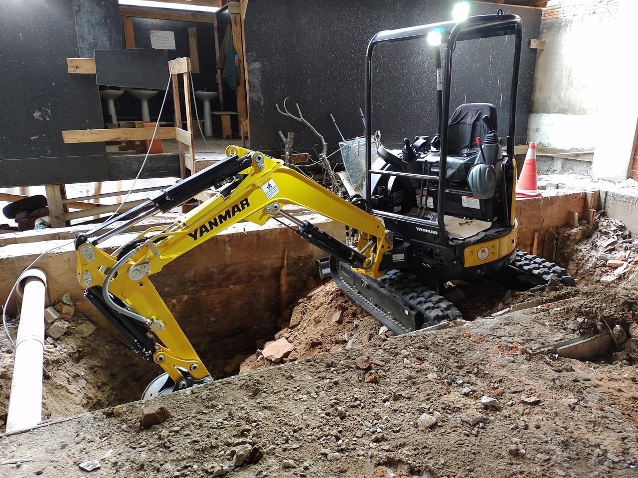 Mini escavadeira trabalhando em escavação no interior de uma construção