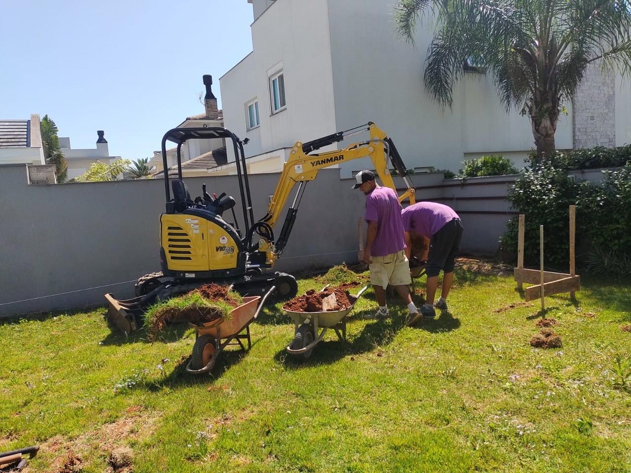Equipe e mini escavadeira trabalhando em jardim residencial