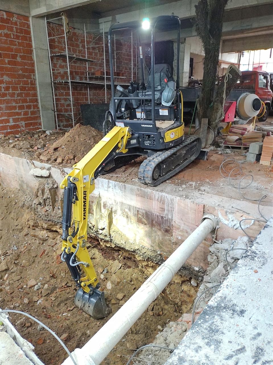 Mini escavadeira abrindo uma vala em construção